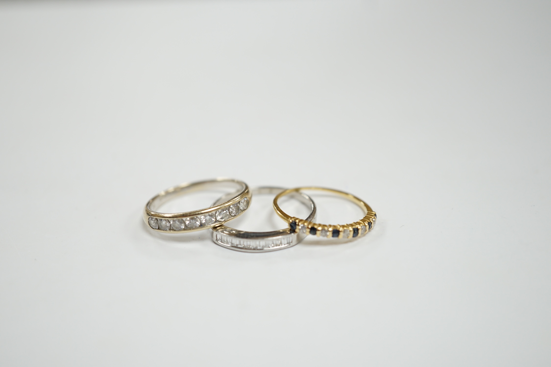A white metal (stamped 950) and thirteen stone channel set baguette cut diamond ring, size O, together with two other unmarked gem set rings including diamond half eternity ring.